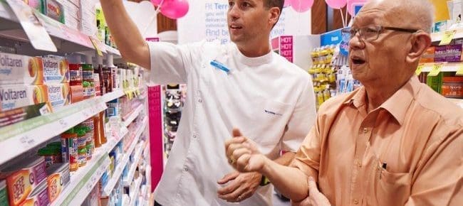 pharmacist helping older patient in pharmacy aisle way