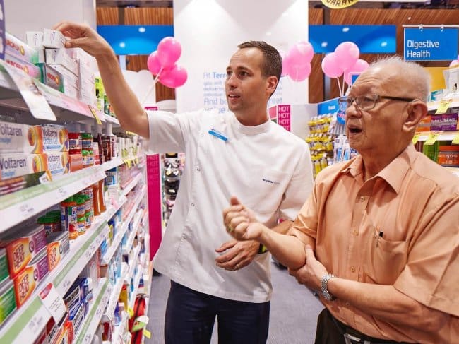 pharmacist helping older patient in pharmacy aisle way