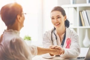 Physician assistant holding female patient hand and pink ribbon
