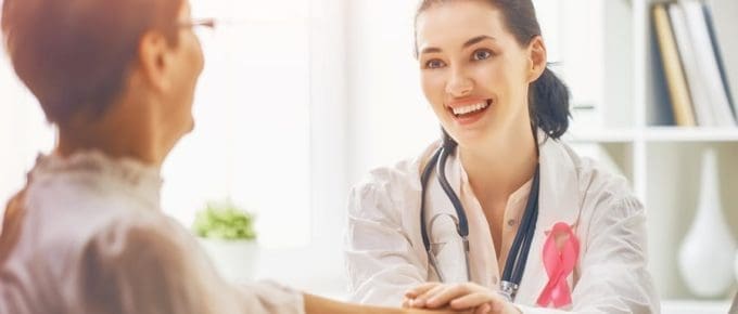 Physician assistant holding female patient hand and pink ribbon