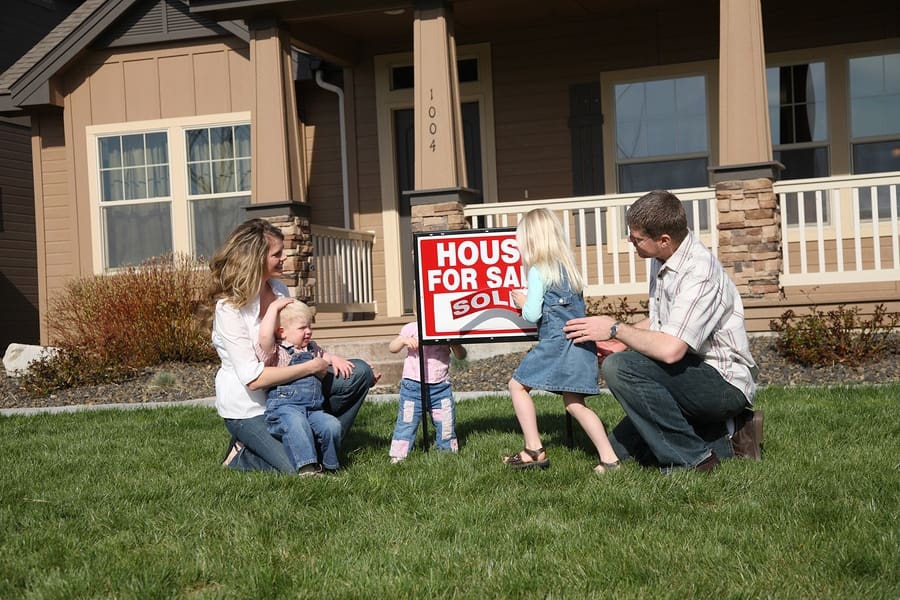 mom and dad with three kids in front of house with sold sign