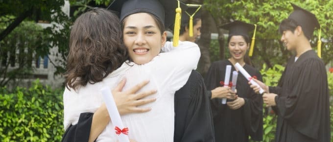 female graduate in cap and gown hugging female