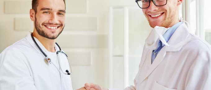 two white male Drs shaking hands in white room