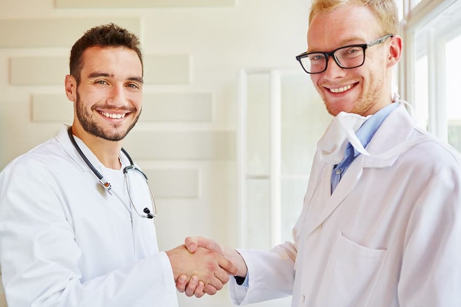 two white male Drs shaking hands in white room