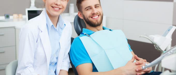 female Dentist working on male patient in dental chair smiling