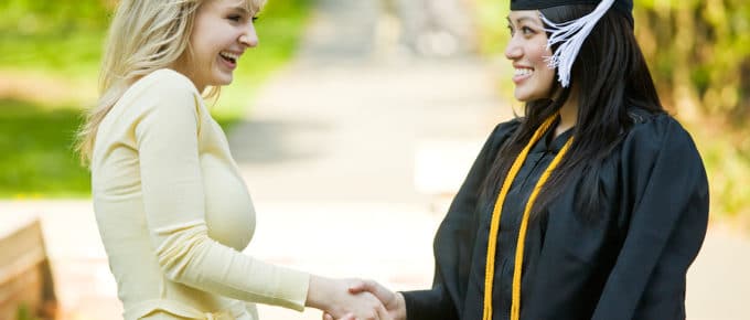 female in graduation hat and gown shaking friends hand