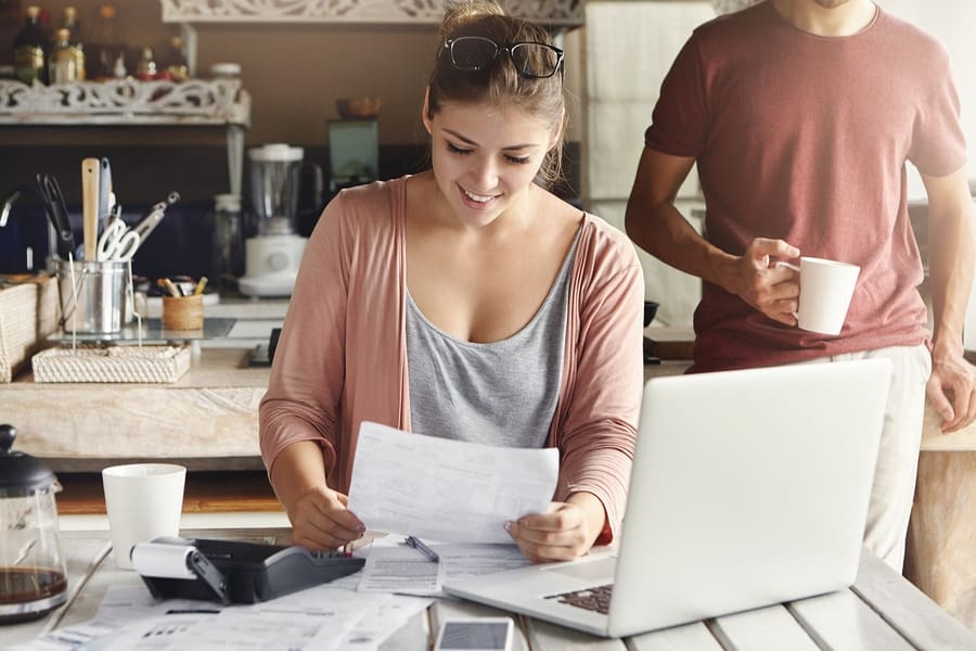 female looking happily at document with male in background drinking coffee