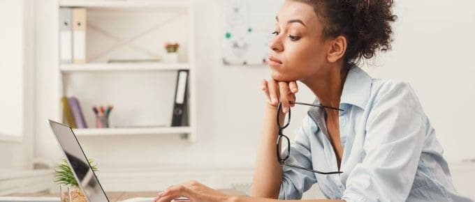 female at desk holding glasses looking at laptop