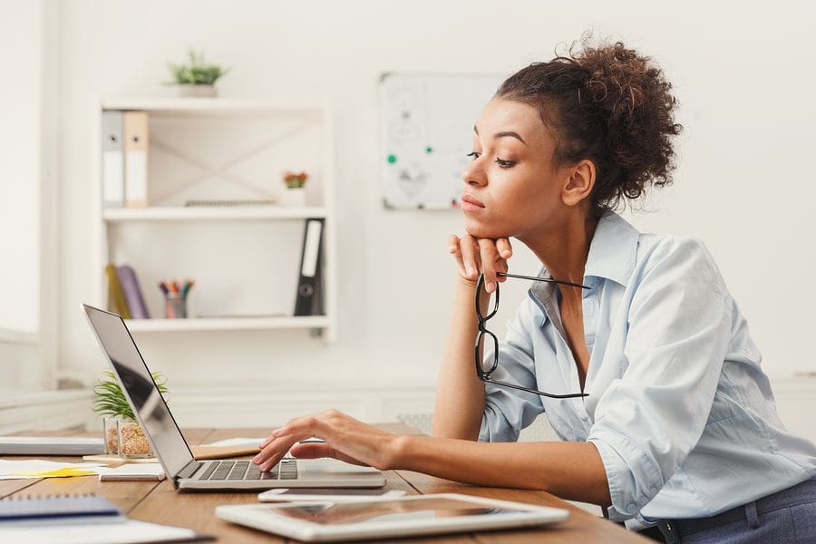 female at desk holding glasses looking at laptop