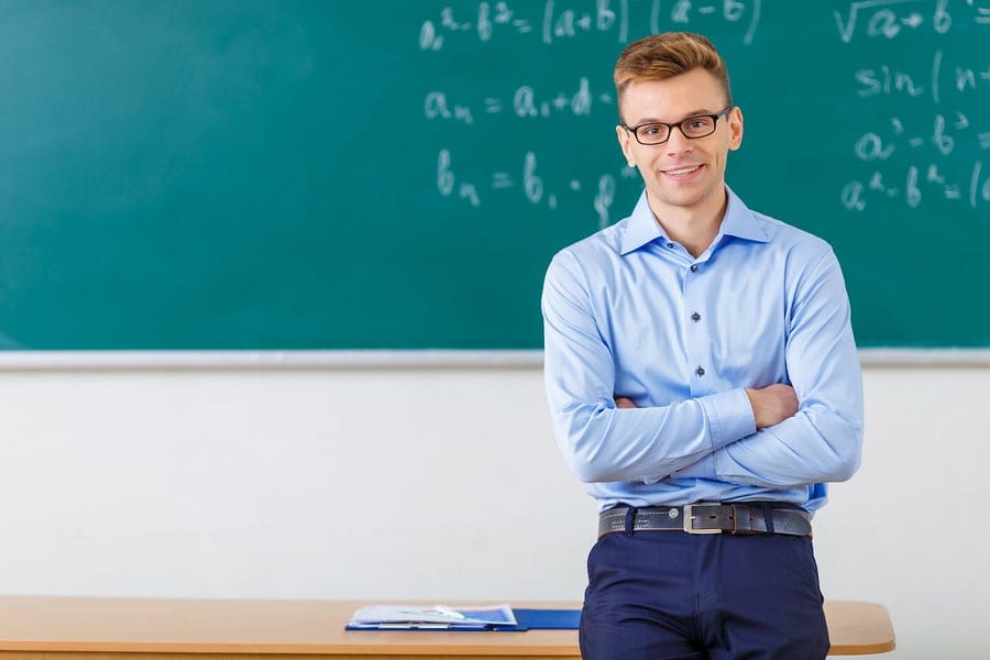 Male teacher arms folded in front of chalk board