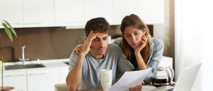 male and female couple looking frustrated at paperwork and computer