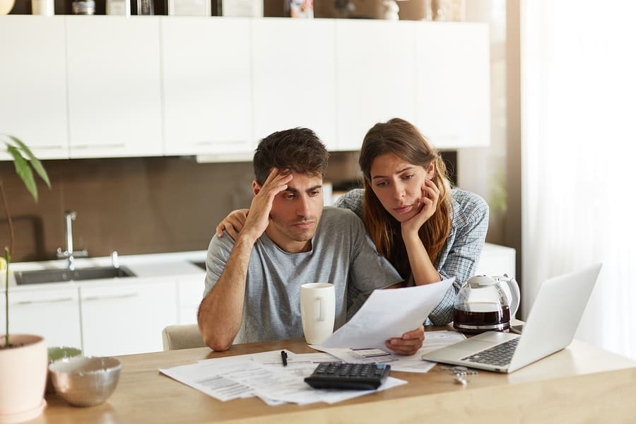 male and female couple looking frustrated at paperwork and computer