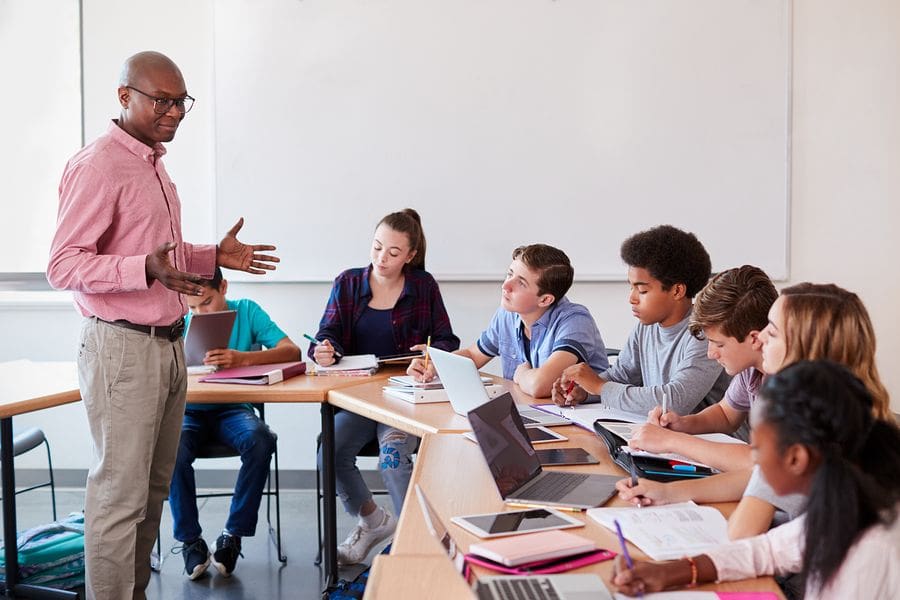 male teacher standing in classroom with seven students