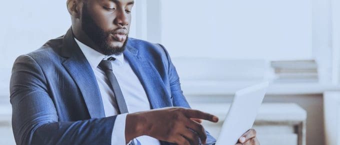 man in suit and tie at desk looking at ipad