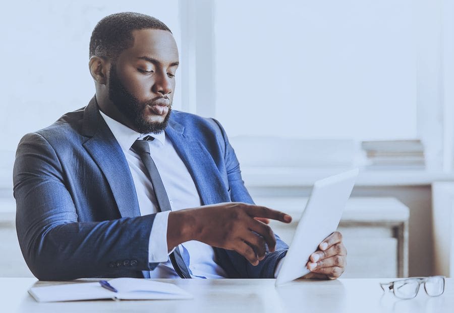 man in suit and tie at desk looking at ipad