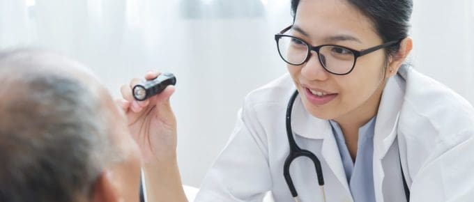 female resident using flashlight to look into male patient eye