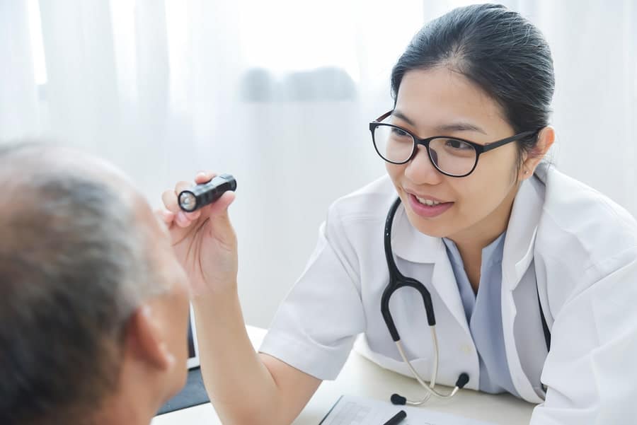 female resident using flashlight to look into male patient eye