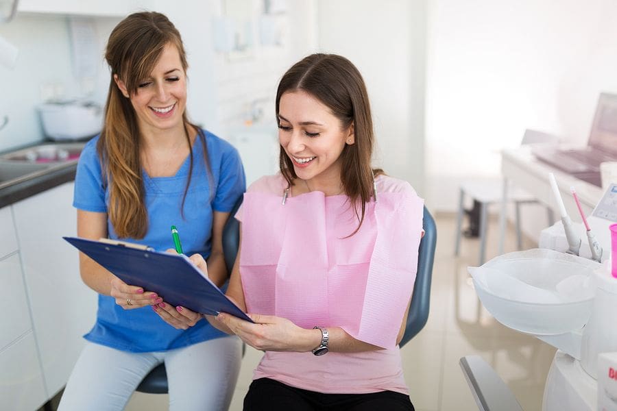 female dentist handing clipboard to female patient in dentist chair