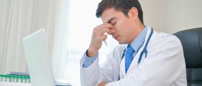 Male Dr. at laptop holding face in frustration