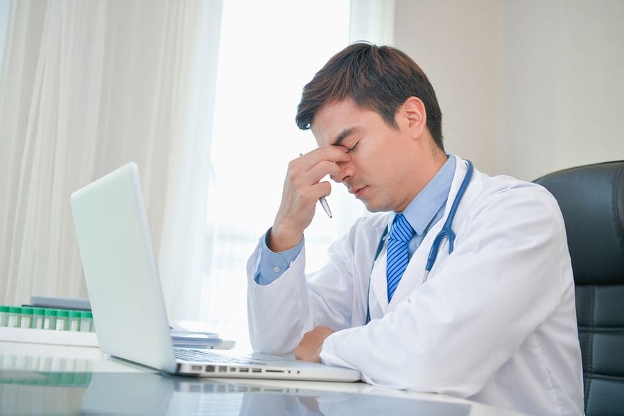 Male Dr. at laptop holding face in frustration