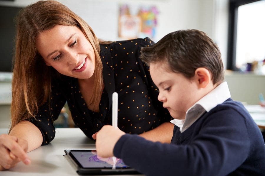 young female teacher helping young boy with ipad