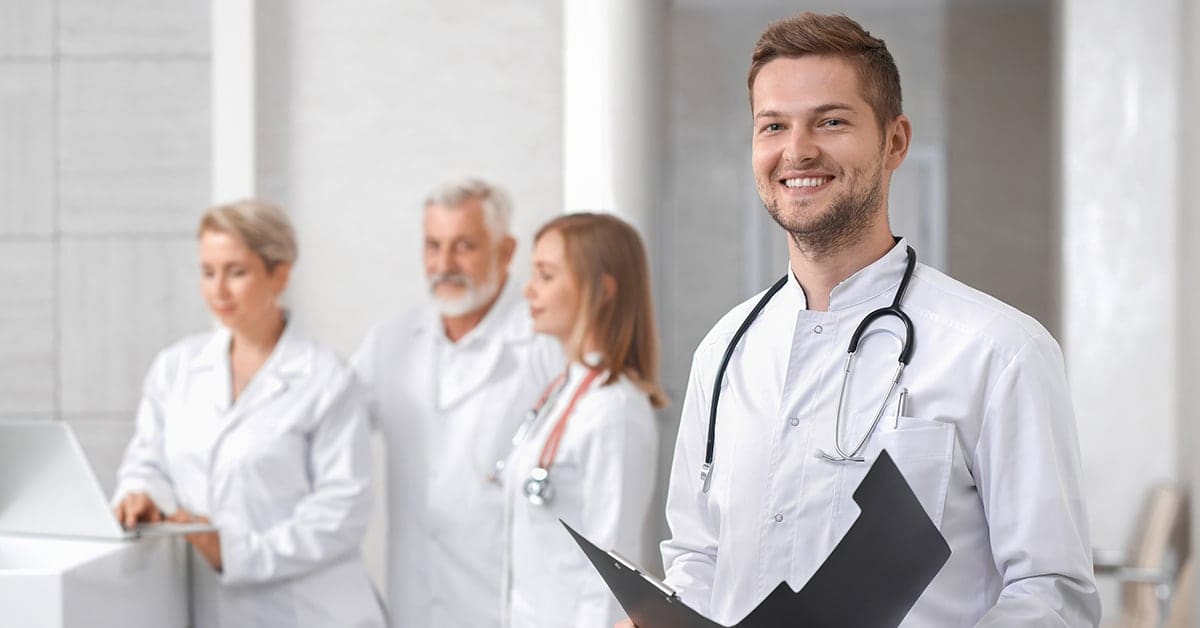 male doctor smiling with group of doctors in backgound