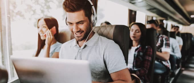 young man smiling with laptop and headphones on bus