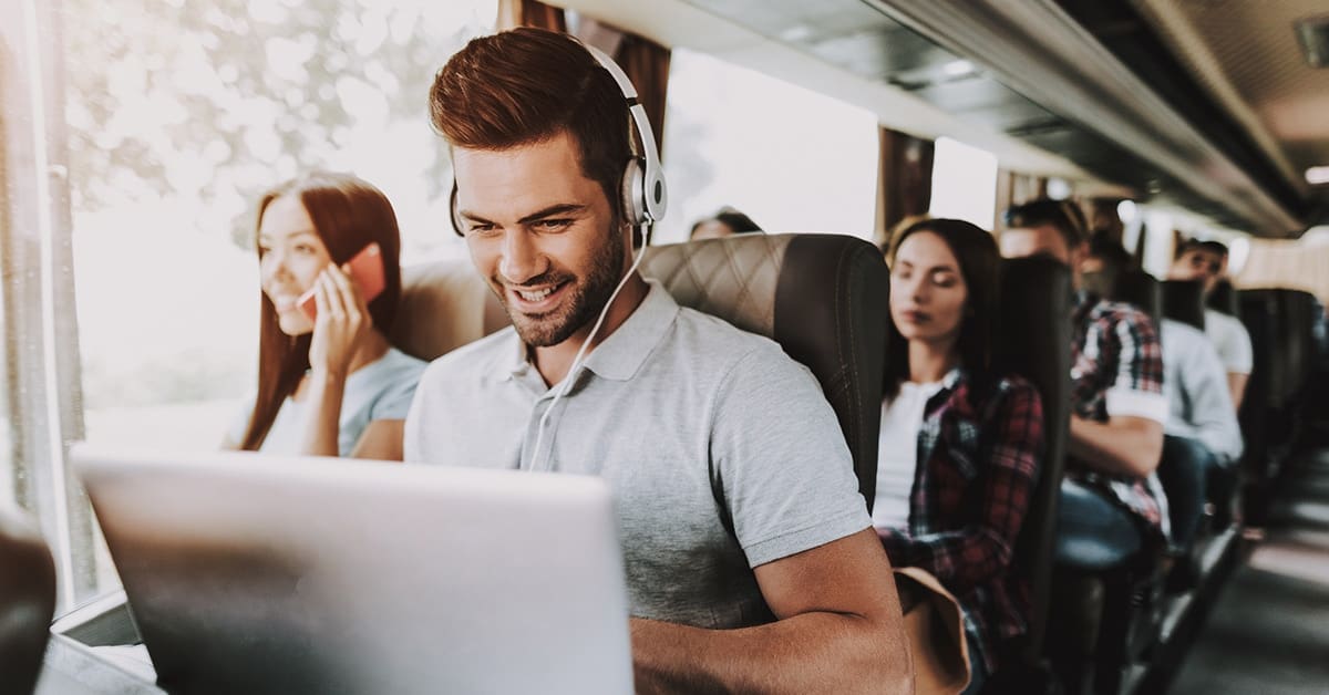 young man smiling with laptop and headphones on bus