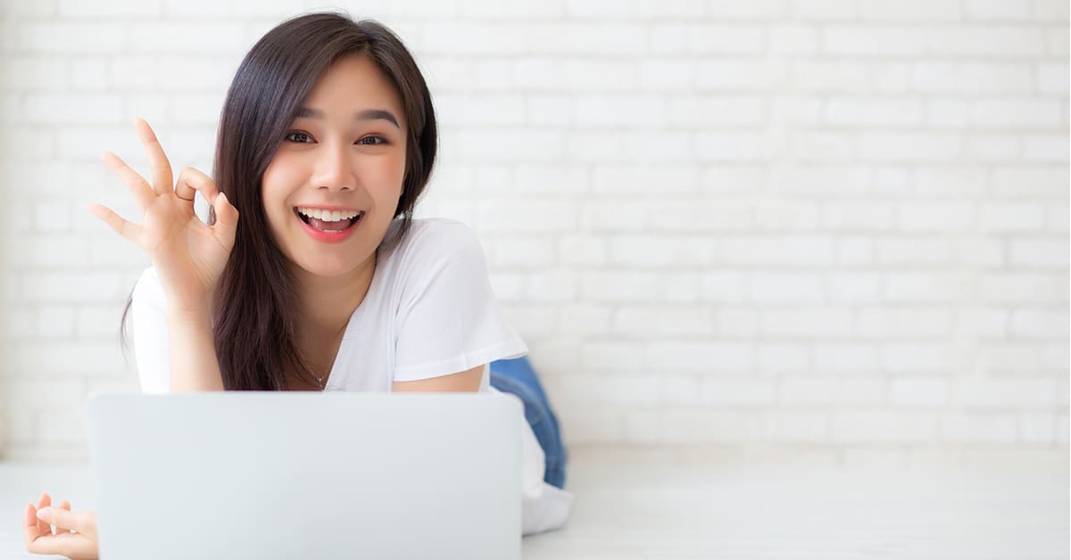 smiling-woman-lying-behind-laptop-ok-sign