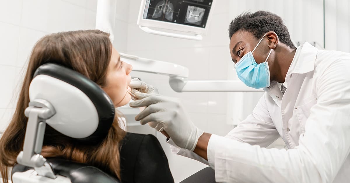 male-dentist-examining-female-patient-mouth