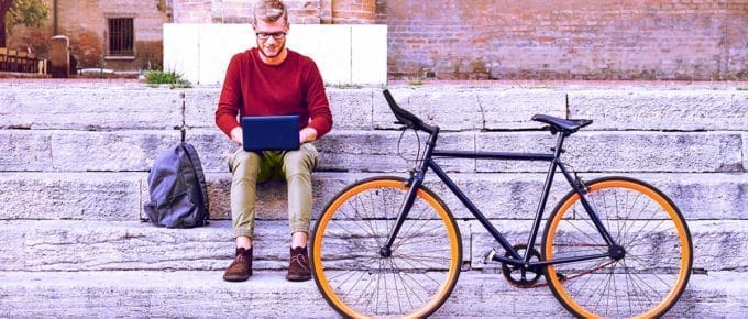 man-sitting-on-steps-outside-laptop-with-bicycle