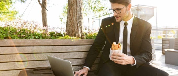 businessman-working-park-bench-laptop-holding-sandwich