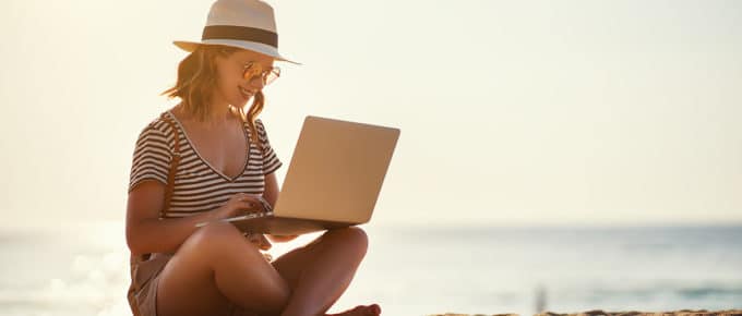 young-woman-sitting-ocean-beach-working-laptop