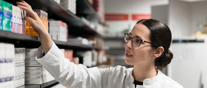 woman-pharmacist-reaching-for-medication-pharmacy-shelves