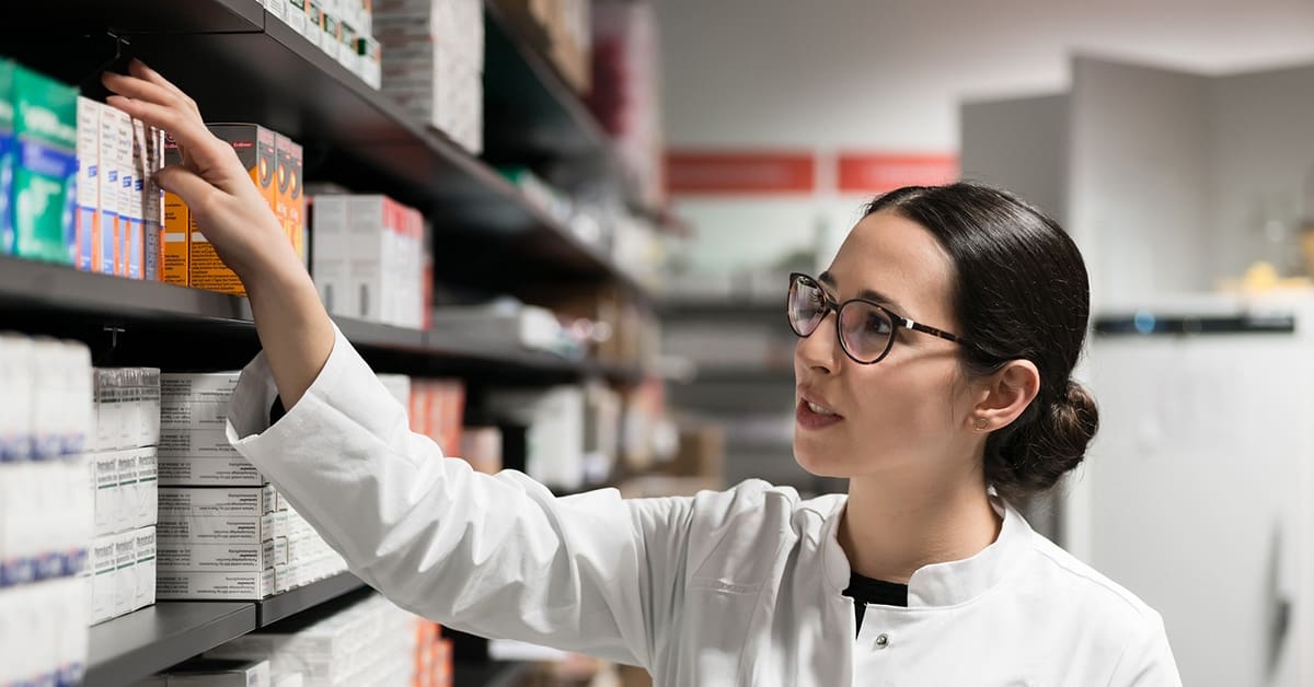 woman-pharmacist-reaching-for-medication-pharmacy-shelves