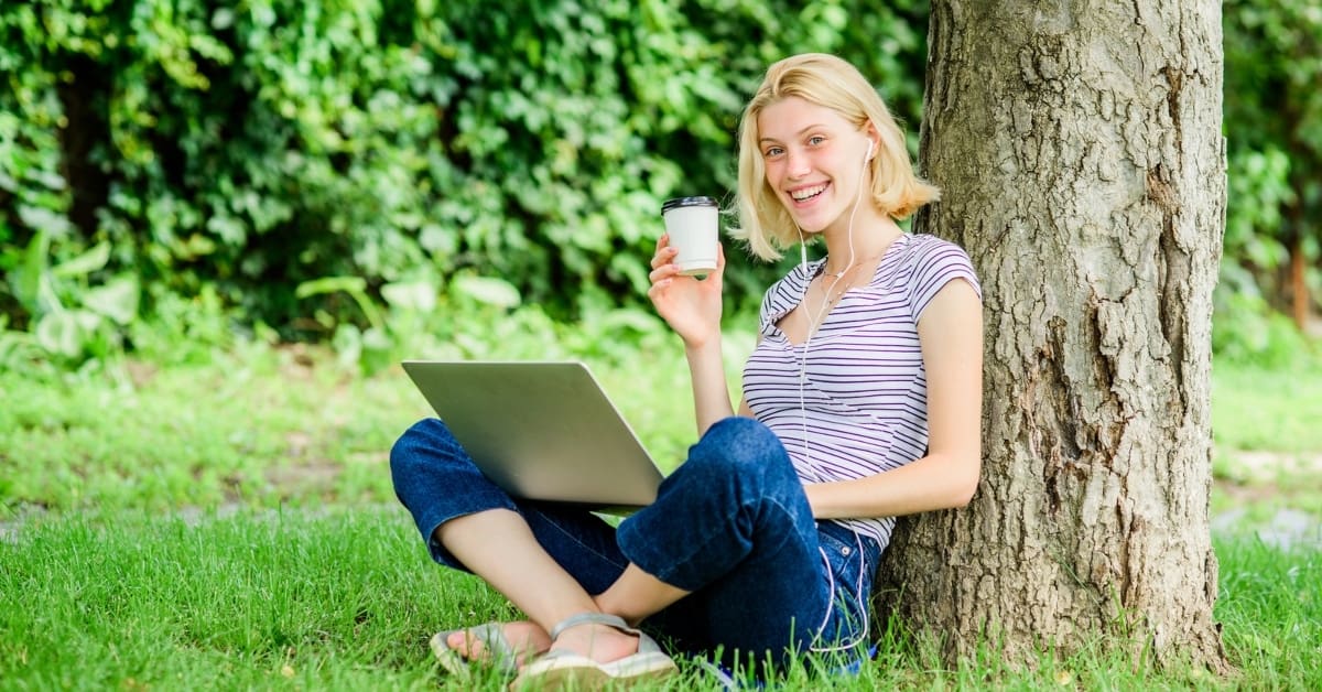 female sitting under a tree on laptop with coffee