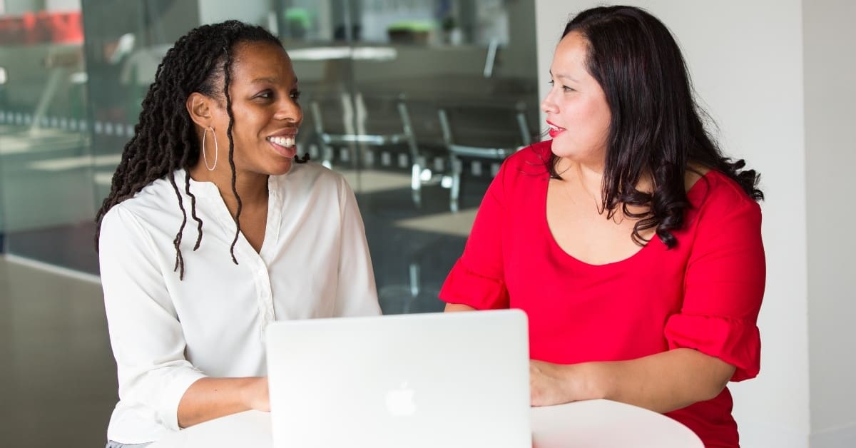 Two Women Looking at Each Other While on Laptop