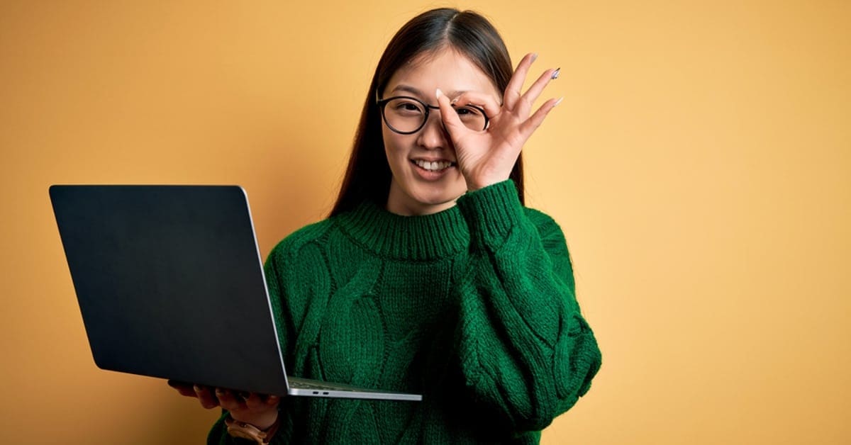 Asian Woman in Green Sweater on Laptop - Orange Backdrop
