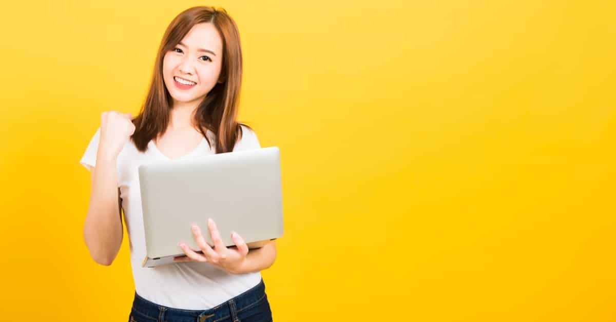 Asian Woman Doing Fist Pump Holding Laptop - Yellow Backdrop