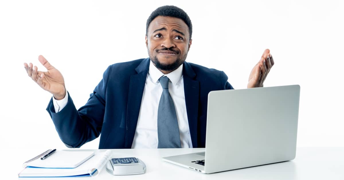 Man in Suit Shrugging at Desk with Calculator and Laptop
