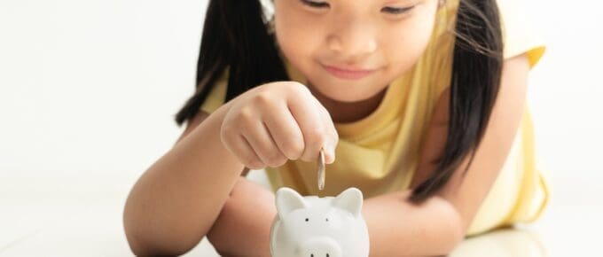 Asian Little Girl Putting Coin in Piggy Bank