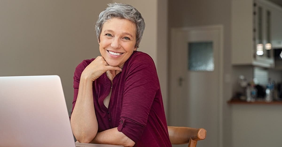 Older Woman Smiling for Camera in Front of Laptop