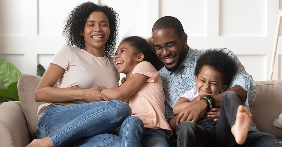 Family of Four Smiling Cuddled up on Couch