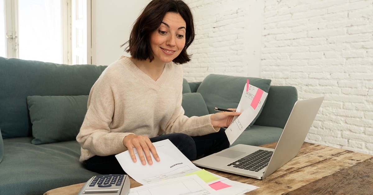 Woman Smiling Over Papers, Calculator, and Laptop