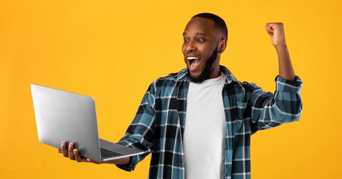 Man Celebrating While Looking at Laptop - Yellow Backdrop