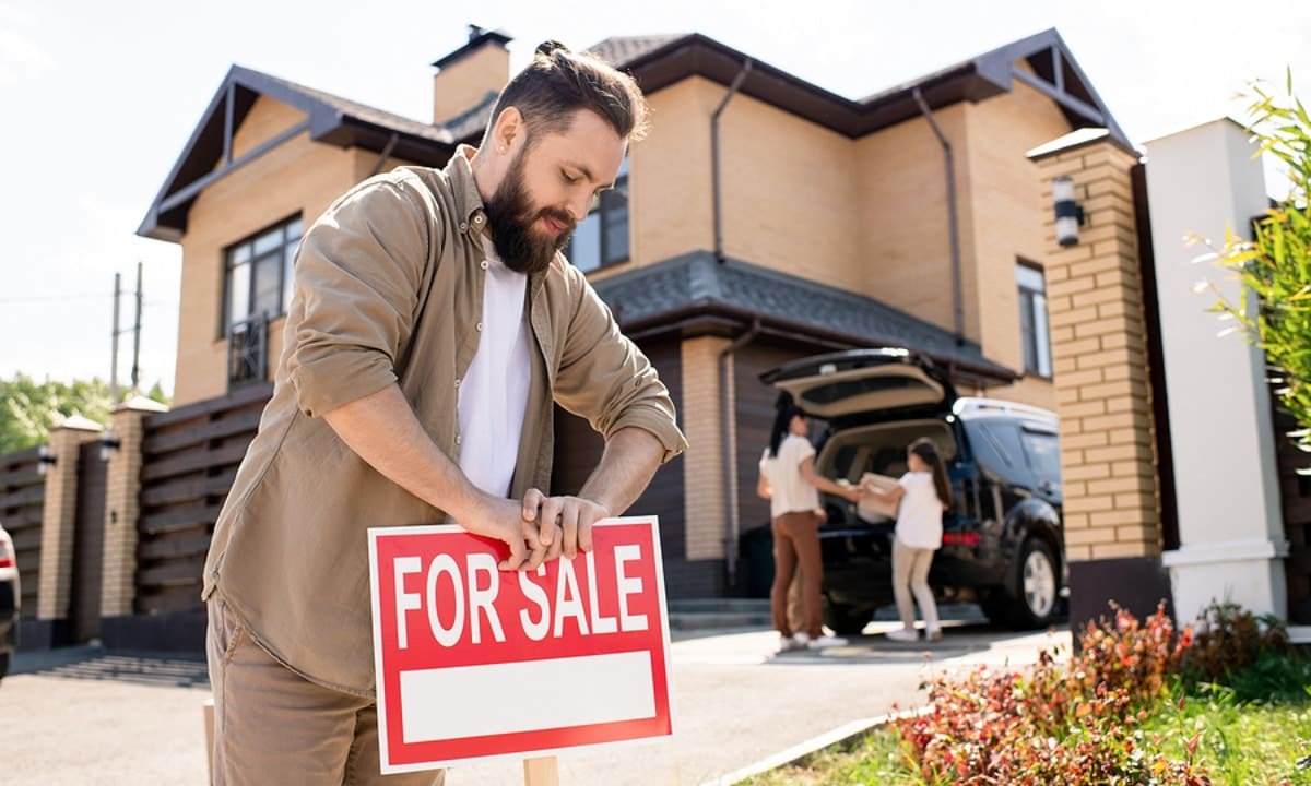 youn bearded guy putting for sale sign out in front of house
