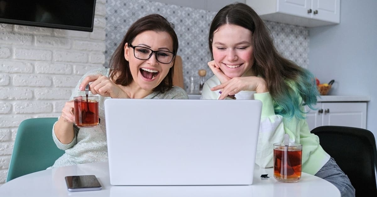 Two Women Rejoicing in Front of Laptop and Drinking Iced Teas