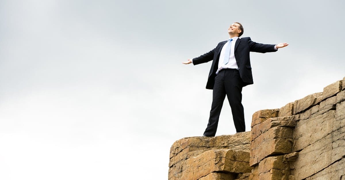 man in suit with arms wide on edge of cliff smiling