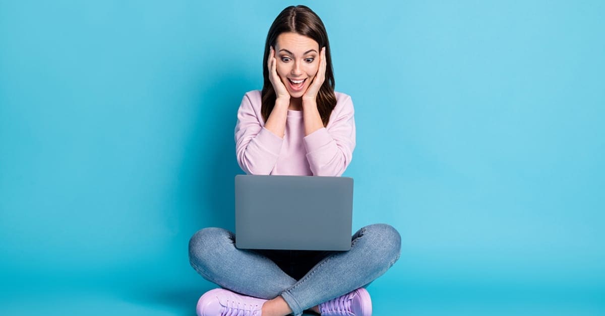 Woman Sitting Crisscross on the Ground Looking at Laptop Smiling