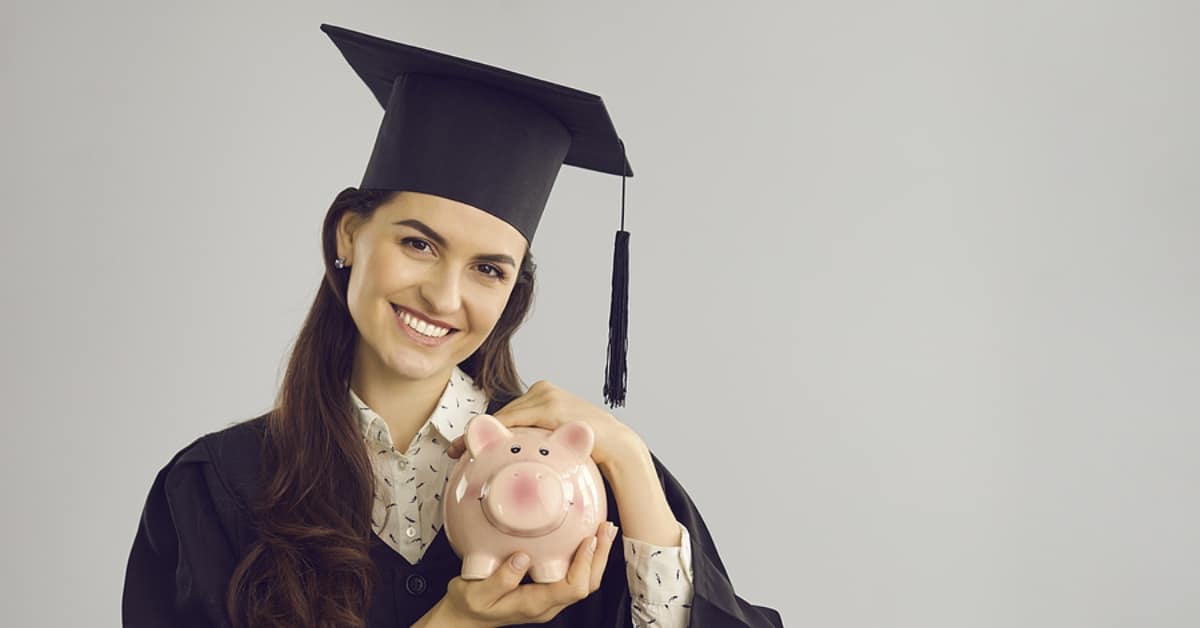 Woman with Graduation Cap and Gown Smiling While Holding Piggy Bank